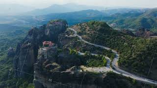 Aerial perspectives reveal cars winding along a road next to a monastery atop a Meteora rock [upl. by Etem]