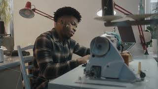 African American seamstress sits at sewing machine by the table with laptop [upl. by Solhcin50]